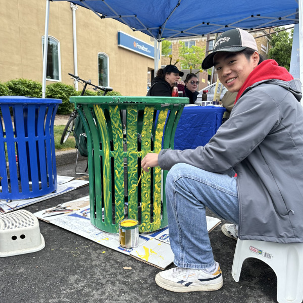 A man painting a curbside trash bin with spring colors.